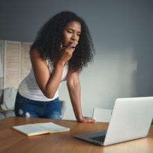 People, lifestyle, modern technology, job and occupation concept. Portrait of beuatiful young African female writer feeling worried, experiencing creative block, using laptop and making notes