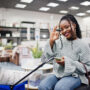 African woman with mobile phone and shopping basket in a modern home furnishings store.